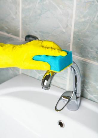 pandemijska dezinfekcija čovjek u žutim rukavicama čisti slavinu za kupaonicu, a spremačica za umivaonik i umivaonik u žutim zaštitnim rukavicama pere prljavu slavinu za umivanje ili umivaonik ruke pere ili čisti kupku izbliza