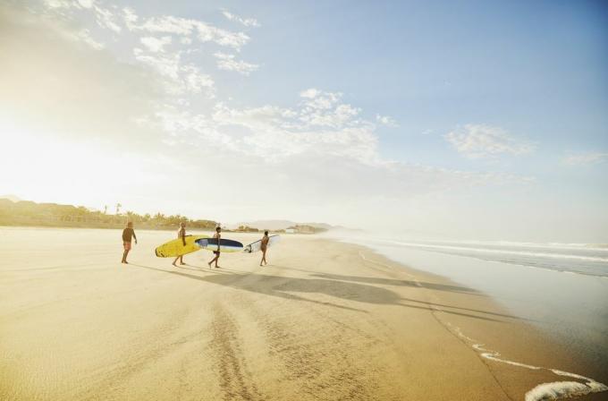Ekstremno široka snimka obitelji koja nosi daske za surfanje na tropskoj plaži dok ide na sat surfanja tijekom odmora