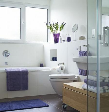 Jasno osvijetljena kupaonica s ljubičastim ručnikom na boku i presavijeni ručnici kraj tuša