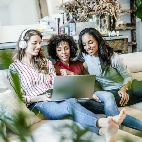 Tri sretne žene s laptopom sjede na kauču