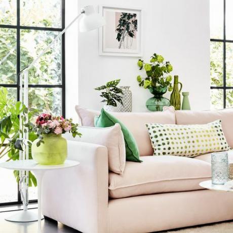 ružičasti kauč u bijeloj sobi sa zelenim biljkama oko sebe i jastucima sa zelenim uzorkom