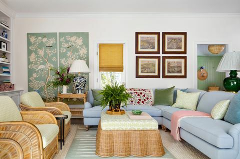 engleska soba, plavi kauč na razvlačenje, pleteni stolić sa zeleno -bijelim jastukom i zeleno -bijelim ukrasnim jastucima, ružičasti tepih, velika zelena lampa