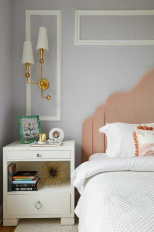 spavaća soba, krevet s bijelim platnom, bijeli pomoćni stolić za krevet, knjige, ružičasto uzglavlje, bijele i zlatne svijećnjake, bijela krošnja na svjetlo sivo plavo obojenim zidovima