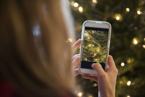 Žena fotografira božićno drvce mobilnim telefonom