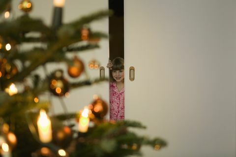 Djevojka u pidžami zaviri kroz vrata u božićno drvce