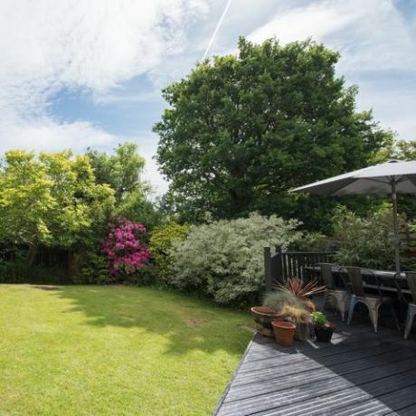 općeniti pogled na stražnji vrt sa sivim podom s vrtnim stolom i stolicama za sunčanog dana u kući